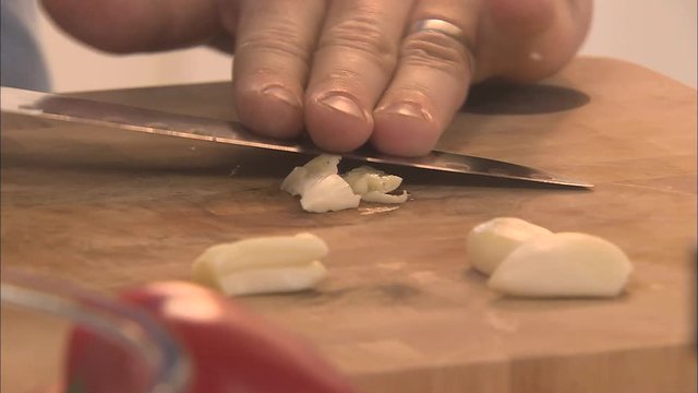 A man crushing a clove of garlic using a knife at home in the kitchen
