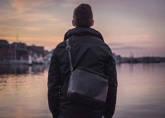 Young traveler with a leather bag from behind looking at the sea during sunset.