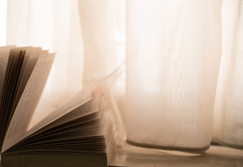 Open book on winodw sill, with curtains and warm light