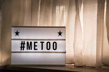 #metoo on lightbox on window sill, with curtains and warm light - copyspace