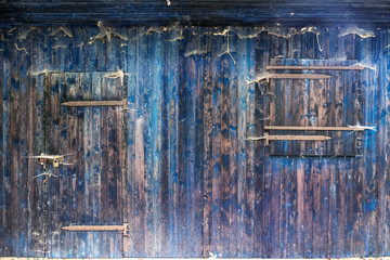 blaue Holz Bretterwand enes Schuppens mit verschlossenem Fenster und verriegelter Tür  mit rustikaler Holzmaserung und vielen Spinnennetzen