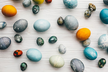 Stylish easter eggs on white wooden background, flat lay. Modern easter eggs painted with natural dye in blue, grey, yellow marble color. Happy Easter pattern, greeting card