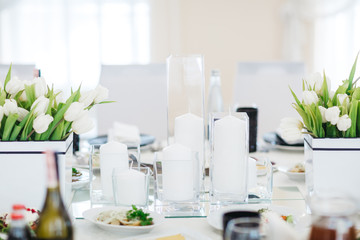 Dinner table serving. White tulips stand in flowerpots on white table served with delicious food