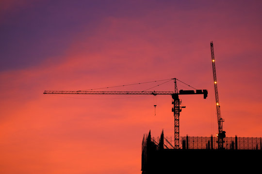 Crane and building construction site at sunrise. High-quality stock photo image silhouette of construction tower crane group with sunset sky background. Building construction with crane during sunrise