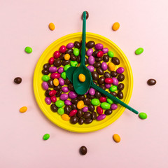 Bright candies dragees on a yellow plate with green spoons