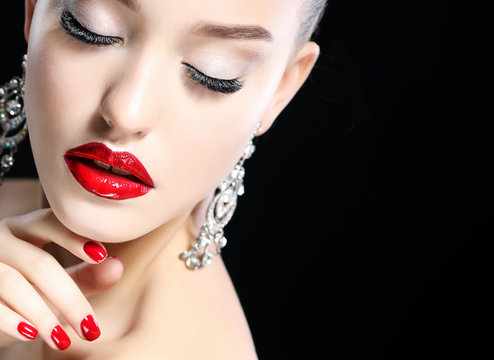 Portrait of young beautiful woman with evening make up touching her face over black background. Red lips and nails.