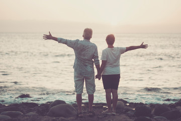 Valentine's day love couple concept with senior aged people open arms with ocean and sunset in front of them - together forever in relationship and married - absolute romantic and romance feel