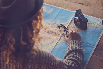 Curly lady viewed from rear planning next trip vacation wanderlust on a paper map and old camera on...