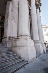 Large white columns of an old architectural building exterior. The building seems to have a brilliant architecture and is pretty old. The clear blue sky can be seen on the background.