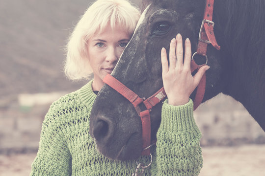 blonde beautiful caucasian model woman with black amazing horse stay together in friendship in fashion style picture concept outdoor nature - hug with love for friends human and animal