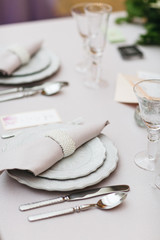 Dinner table serving. Violet and beige tones, pastel colors. Beautiful decoration of wedding banquet in restaurant with glasses, plates, forks and knives, white tablecloth.
