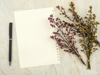 Top view of note pad paper with pen and group of bouquet dried and wilted multiple color Gypsophila flowers on matt marble background for text, letter, message or verse