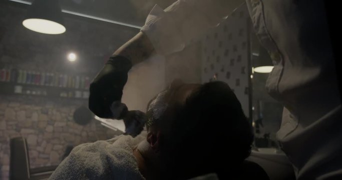 Barber applying foam for shaving to male client in Barbershop slow motion