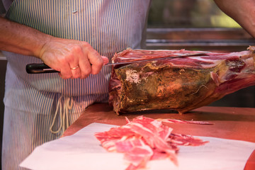 A butcher is seen cutting beef meat with a butcher knife. The meat looks fresh and is ready to be sold after being cut. He is seen wearing a stripe Apron.