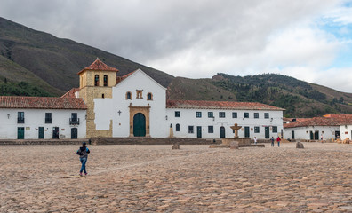 People crossing Villa De Leyva famous colonial central square “Plaza Mayor”, cobblestone covered, in Boyaca, Colombia