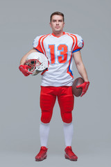 American football player holding rugby ball and helmet against grey background full length © satyrenko