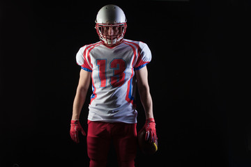 American football player wearing helmet posing with ball on black background