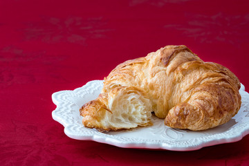 Fresh croissant on a white stoneware plate on red tablecloth