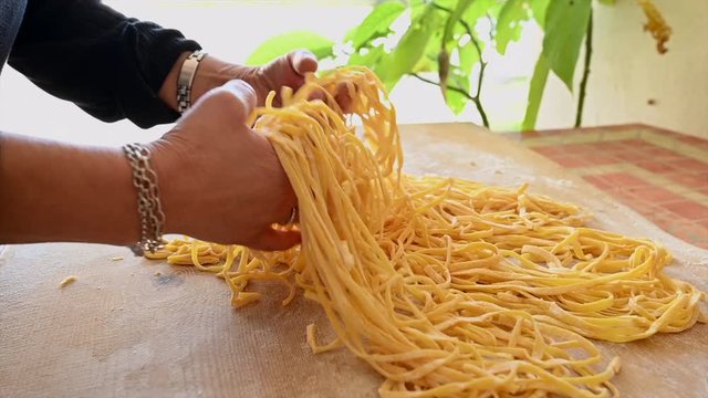 An Italian woman is preparing a fresh pasta called 'Fettuccine' made from fresh eggs and durum wheat flour. Fettuccine is a flat thick pasta popular in Roman and Tuscan cuisine.
