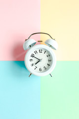 White alarm clock on colorful background. Trendy minimal style. Beauty and fashion concept. Flat lay composition. Top view.