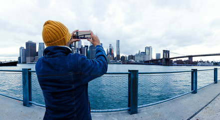 Asian traveler taking photo with mobile phone in Brooklyn bridge at sunset. New York city.
