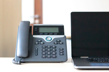 Black VoIP telephone on desk with computer laptop