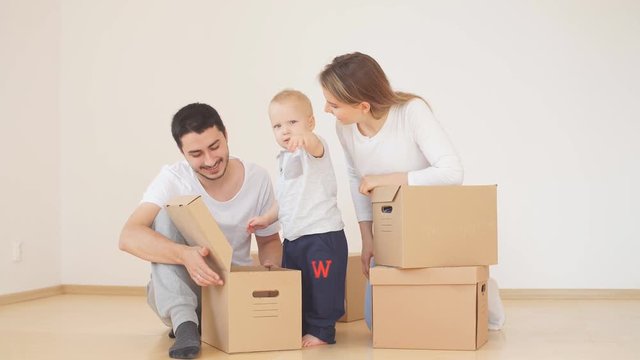 Family with little boy unpacking moving cardboard boxes at new home