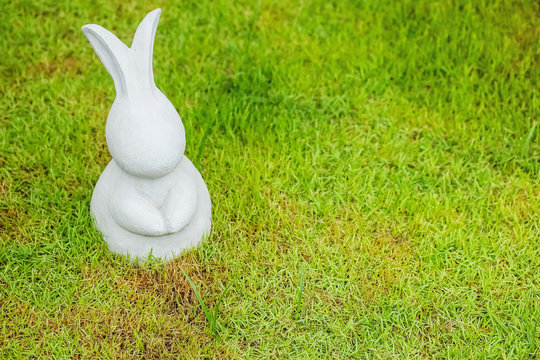 Closeup cement rabbit statue for decoration on grass floor in the garden background with copy space