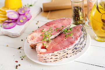 Raw steak of carp fish with lemon and thyme  on white wooden background. Preparing fish for roasting in parchment paper. Diet menu.