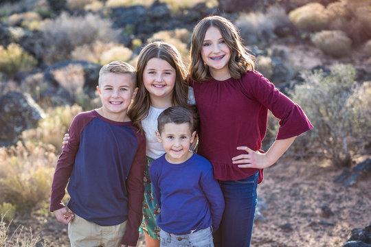 Beautiful Portrait of smiling happy kids outdoors. Four siblings standing together for a cute picture. One teen girl and three younger kids