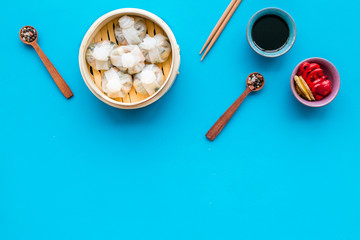 Dim sums with red pepper and vegetables with sticks and black tea in Chinese restaurant on blue background top view mockup