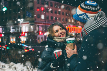 Real young couple walking together in night city under snow, kissing and sm