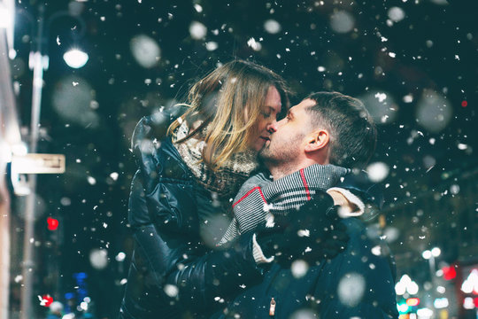 Real Young Couple Walking Together In Night City Under Snow, Kissing And Sm