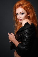 Portrait of young sexy redhead girl in leather jacket on dark background in studio