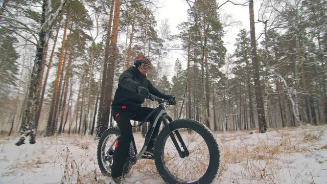 Professional extreme sportsman biker sit a fat bike in outdoors. Cyclist recline in the winter snow forest. Man walk with mountain bicycle with big tire in helmet and glasses. Slow motion in 60fps.