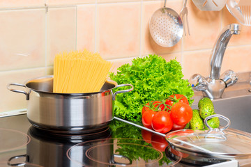 pan with spaghetti and fresh vegetables in the kitchen near the sink