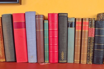 Wooden shelf with historic,decorated, vintage books. Old books on yellow and claret background