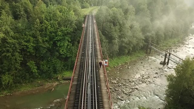 Aerial footage of a woman walking on the tracks of a railway bridge over the Prut River in Yaremche, the city on the Carpathian Mountains in Ukraine.