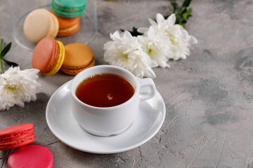 Provence breakfast. Bright french macarons on a round plate, a cup of tea, a teapot. Grey background.