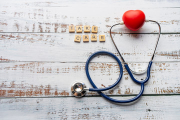 Letters take care on grain wood with red ball heart shape and  stethoscope.