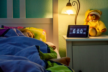 Little girl sleeping in bed - Alarm clock at 6 am in the morning.