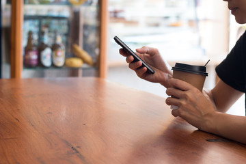 Hands of a woman is holding hot cup of coffee with using a mobile cell phone in coffee's shop, shopping on line concept