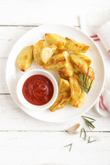 Potato baked and tomato ketchup on white plate, wooden background, top view
