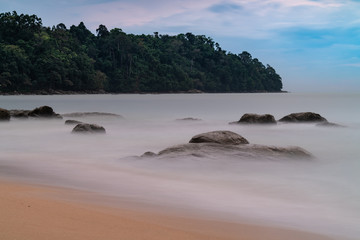 Long exposure of the sea with rocks surfacing out of the water and tropical vegetation in the background