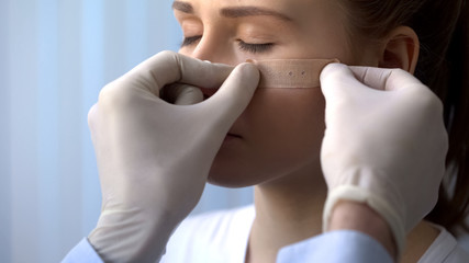 First aid measures, doctor putting patch on wounded female patient face closeup