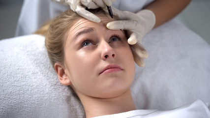 Obraz na płótnie Canvas Experienced cosmetologist marking position of wrinkles on girls forehead