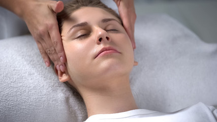 Obraz na płótnie Canvas Beautician making relaxing facial massage, rubbing rejuvenating serum to woman
