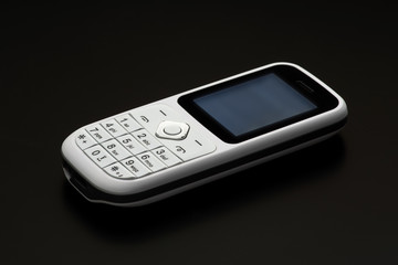 White push-button mobile phone of the old model on a black background