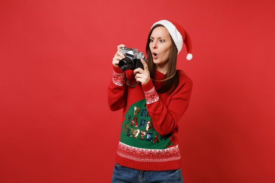 Shocked young Santa girl taking pictures on retro vintage photo camera, keeping mouth wide open isolated on red background. Happy New Year 2019 celebration holiday party concept. Mock up copy space.