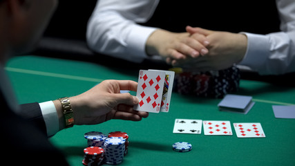 Businessman playing poker at casino checking combination of cards, gambling